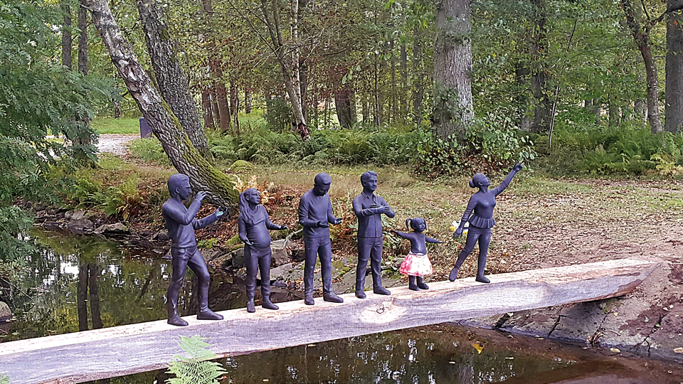 Konstverket Alla är. Små skulpturer placerade på träplanka placerad över vatten 