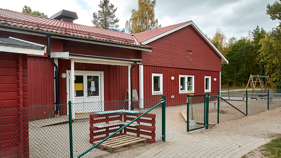 Ett rött trähus med rött tak. Bredvid förskolan finns en skolgård med en gungställning. 