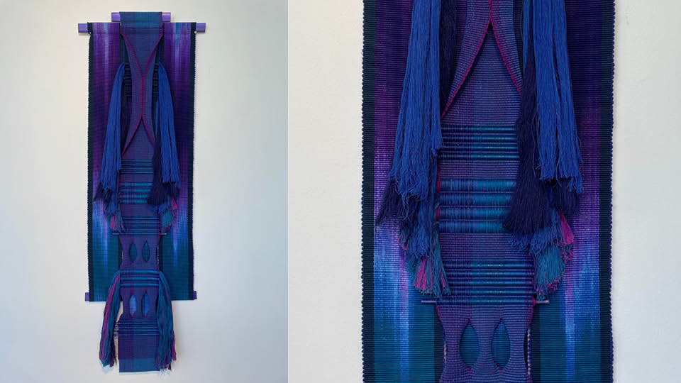 Foto på ett avlångt textilt verk med långe toffsar. Går i färgerna blått lilla och mörkt turkos.