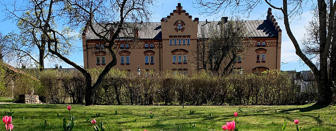 Orange tegelbyggnad, framför byggnaden finns en gräsmatta med rosa tulpaner 