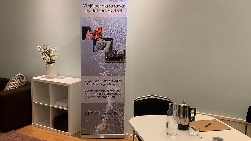Foto på Avskedsbyråns kontor, med en lila roll up och en kaffetermos.